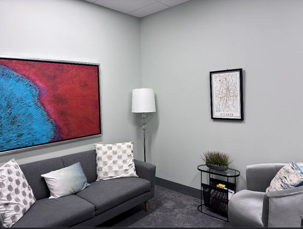 Office 2 with a dark gray sofa, a gray armchair, a floor lamp, and colorful abstract artwork.